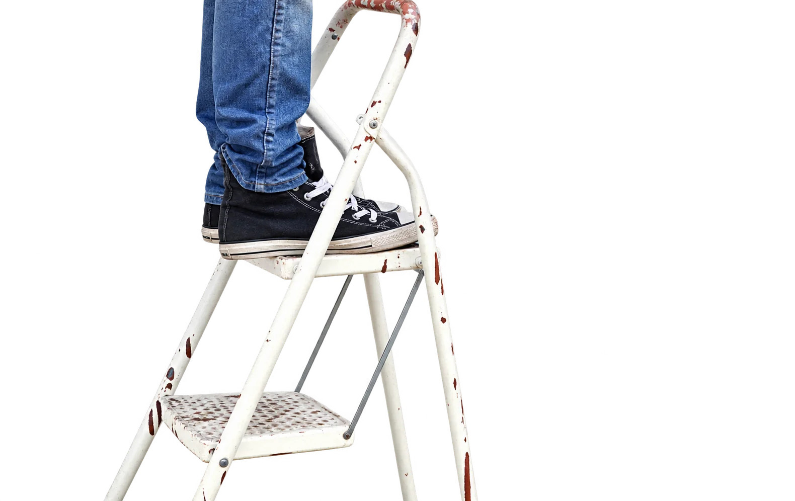 Une personne en jean et baskets noires se tient sur un escabeau métallique blanc devant un mur blanc.